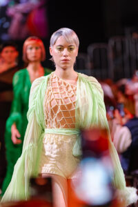 La modella cattura lo sguardo con un taglio moderno e un maquillage che riflette il tessuto traslucido del suo abito, creando un'aura di grazia al Kadus di Bologna