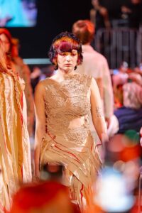 Una modella con un'acconciatura colorata esprime audacia e individualità, indossando un abito che gioca con texture e forme alla sfilata Kadus a Bologna