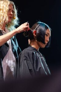 Un parrucchiere esperto modella una pettinatura innovativa, mescolando arte e precisione al Kadus di Bologna.