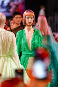 Frammenti di verde esplodono sulla scena mentre una modella in abito verde presenta un taglio capelli moderno e geometrico, accendendo la passerella di Kadus